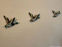 Wide view of all three wall-mounted ceramic ducks in flight, arranged on wall.