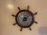 Front view of the vintage ships wheel barometer showing dial and wooden wheel frame.