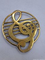 Front side view of the solid brass ampersand trivet showing the polished gold finish and detailed ampersand design on circular base with horizontal bars.