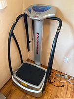 Full view of the T-Zone vibration machine showing the frame, black textured platform, and control panel with handles.