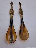 Front view of the salad servers showing pronged fork and spoon heads in brown resin with brass handles
