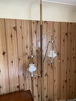 Full view of the vintage pole lamp showing the two hanging lamps with milk glass shades and wooden finials against a wood panel wall.