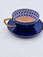 Teacup and saucer set showing the overall cup shape, woven handle, and dark blue exterior with decorative interior.