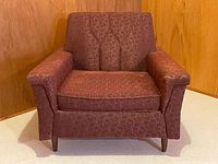 Front view of vintage upholstered chair showing angled arms, patterned fabric, and wooden legs