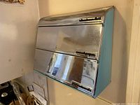 Front view of dispenser showing two chrome lids and aqua body