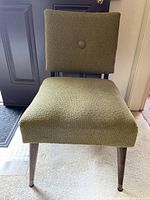 Front view of vintage green chair showing seat, back and tapered wooden legs with metal caps