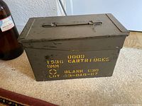 Photo of green metal military ammunition box with yellow stenciled text and metal handle