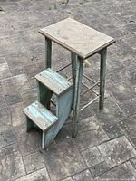 Front view of the vintage wooden step ladder with nested steps and worn green paint.