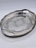 Full view of the oval silver plated tray with ornate engraving and pierced gallery sides with handles.