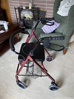 Full view of red walker showing frame, wheels, seat, hand brakes, and basket
