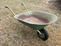 Front angled view of the wheelbarrow showing green metal tub, yellow handles with black grips, and single wheel.