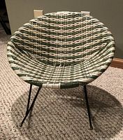 Front view of the vintage child's saucer rocking chair showing the woven plastic-coated rattan seat in green and white with black metal rockers.