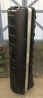 Full side view of the black hard golf travel case standing upright, showing textured exterior and handle.