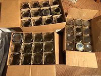 Top-down view of three open cases of mason jars, each separated by cardboard dividers, showing quart, wide-mouth pint and pint jars.