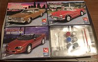Three AMT model car kits displayed showing box art for 1969 Olds 442, 1958 Corvette, and 1993 Camaro Z28. Paint pots and assembly tools visible.