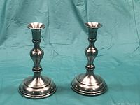 Pair of Yarmouth pewter candlestick holders shown from front against light blue fabric background.