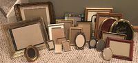 Front view of assortment of picture frames showing variety of sizes, shapes and materials including wood, metal and brass.
