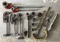 Full layout of the lot showing three pipe cutters (two Ridgid), pipe threading dies, handles, and accessories arranged on concrete floor.