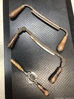 Top view of three spoke shave tools arranged on black textured surface, showing wooden handles and metal blades.