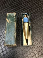 Full view of the brass plumb bob with its green original box, showing wear on the box.