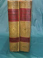 Two volume spines side by side. Gold embossed text with red labels showing titles and volume numbers.