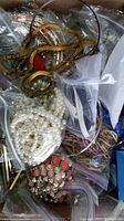 Photo showing mixed costume jewelry with faux pearl necklaces, gold-tone chain bracelets, and various bead necklaces in plastic bags.
