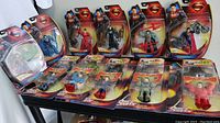 Front view of multiple Superman action figures in original packaging displayed on a table showing several different characters and accessories.