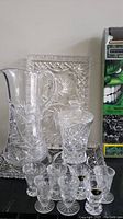 Display of crystal glassware set including pitcher, decanter, plates, and shot glasses alongside Hulk activity desk box