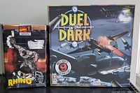 Front view of Duel in the Dark board game box and sealed Marvel Rhino figurine box side by side.