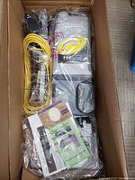Vacuum cleaner and accessories packaged in original box with power cord coiled beside unit.