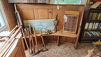 Vintage wooden bench seat placed indoors, showing front view with hunting and fishing decor items on it, partially obstructing seat area to indicate items not included.