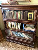 Full view of a wooden three-tier glass bookcase filled with various vintage books and a Kodak film box