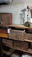 A shelf with various wooden crates including Teacher's Highland Cream Whisky and Western Wire & Nail Company crates alongside a small plain wooden box with door.