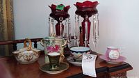 Overview of all items: two ruby glass candle holders, porcelain sugar bowl, lidded jar, demitasse cup set, floral cup set, blue bowl, pink souvenir cup and saucer