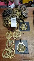 Overview of pile of brass horse ornaments on wooden surface with lot tag visible