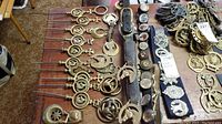 Overview of loose brass horse brasses laid out in rows beside three leather straps with attached medallions