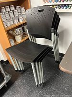 Stack of four stacked black plastic chairs with metal legs and perforated backs.