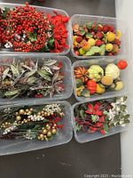 Top-down view of six plastic tubs each containing various seasonal crafting décor such as artificial berries, leaves, small pumpkins, and faux poinsettias.