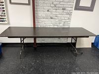 Full front view of the entire 8 ft folding table with dark brown tabletop and metal legs.