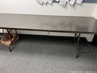 Side view of rectangular folding table showing dark top and metal legs.