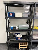 Photo of the black resin 5-shelf shelving unit showing all five shelves with various storage containers on top (contents not included in lot).