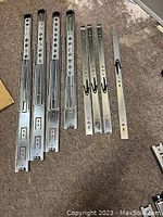 Four single metal drawer slides and three pairs of double metal drawer slides displayed on carpeted floor.