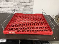Side view of one red bread rack showing lattice plastic base and metal rail sides