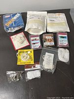 Photo of candle making supplies including beeswax pellets, Parowax blocks, scented wax cubes, various wicks on different packaging cards and in loose bags, and metal wick bases.