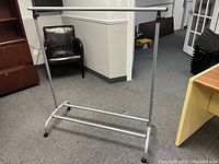 Full view of the silver metal clothing rack with four caster wheels on a carpeted floor.