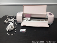 Full view of Cricut Air 2 cutter open with power supply, USB cable, and replacement blades on black table