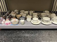 Various cups, saucers, and small plates with different patterns and styles displayed on a shelf.