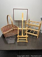 Five display items on a table: large woven wooden basket with handle, smaller wire basket, wooden easel, metal sign holder, and wooden wine rack