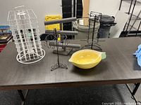 Photo of multiple display racks and a ceramic bowl on table including wire rack, black round rotating stands, and ceramic bowl