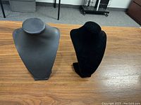 Two free standing necklace displays, one black leatherette and one black velvet, on a wooden table.